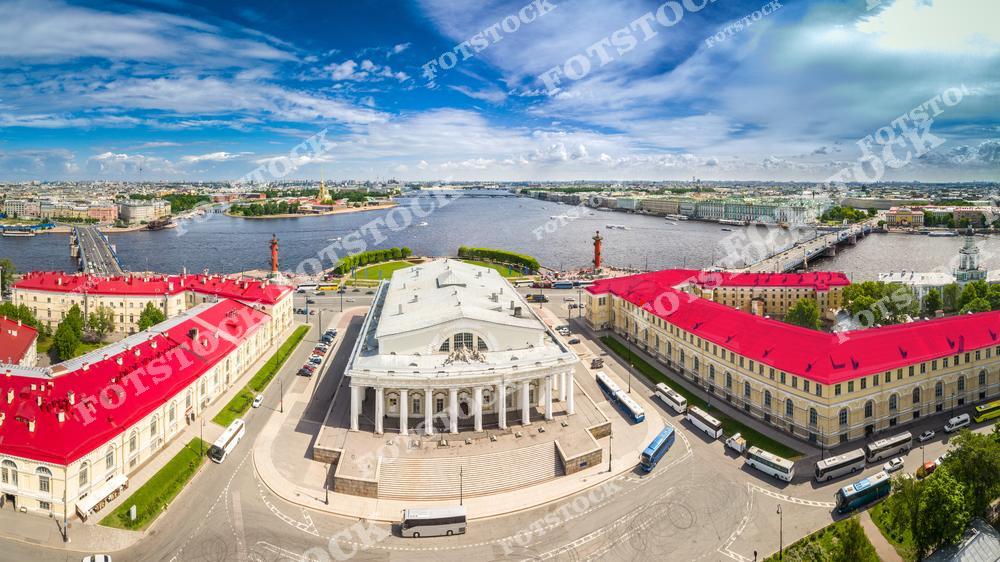 На фотографии изображена Стрелка Васильевского острова — одна из знаковых достопримечательностей Санкт-Петербурга. В центре кадра находится здание Старой Биржи, построенное в начале XIX века в стиле классицизма. По бокам возвышаются Ростральные колонны, служившие маяками для судов. Слева и справа — Дворцовый и Биржевой мосты через Неву. Вид выполнен с высоты и позволяет увидеть архитектурное единство центра города в летний день.
